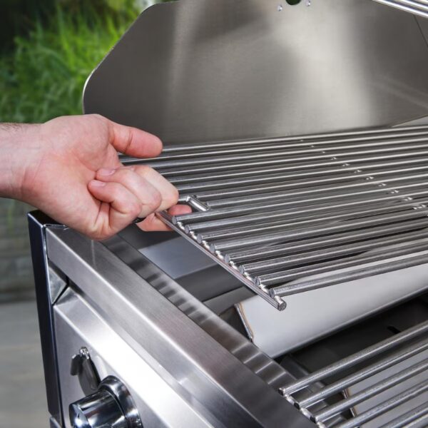 Hand adjusting a stainless steel grill grate inside a modern gas grill, with lush greenery in the background.