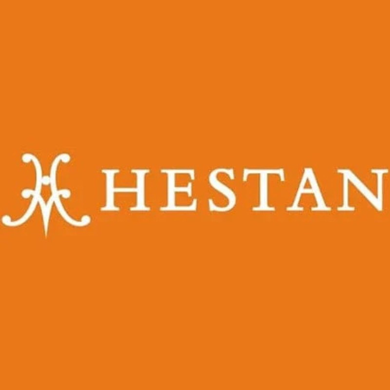 Hestan logo on an orange background, featuring an elegant design with the brand name prominently displayed.