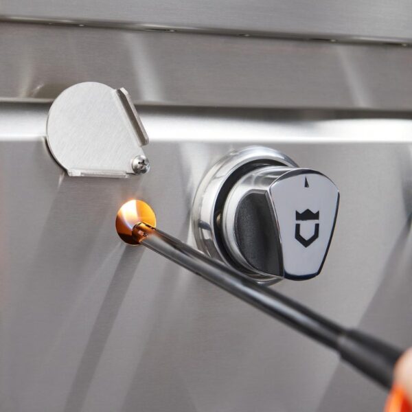 Close-up of a stainless steel grill with a spark igniter being used to light the burner, showcasing the ignition process and control knob.