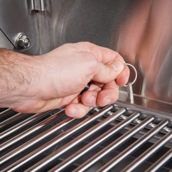 Hand using a metal hook to secure or adjust a grill's cooking grate in a stainless steel barbecue.
