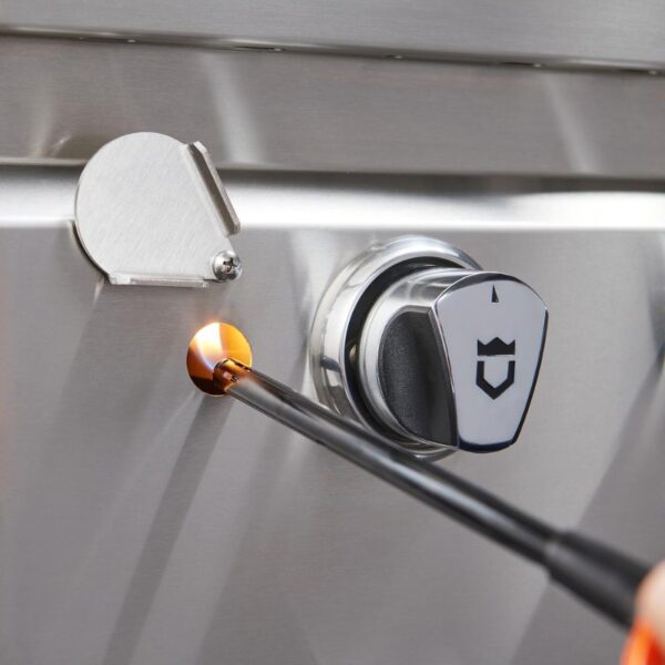 Close-up of a stainless steel grill ignition system, featuring a lit lighter inserted into the ignition port, with a control knob visible nearby.