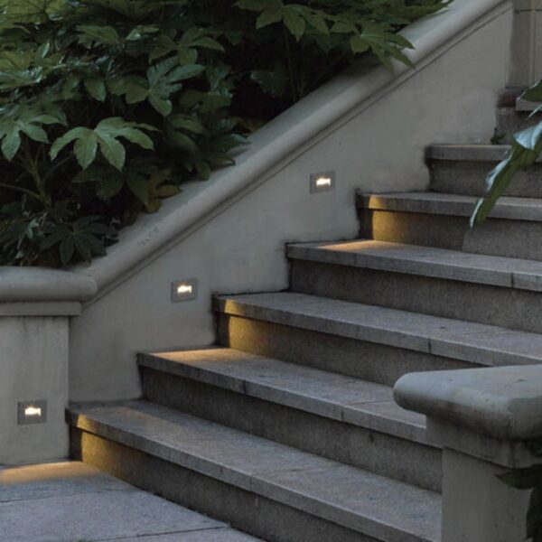 Illuminated outdoor stairs with built-in LED lights along the wall and lush greenery surrounding the area.