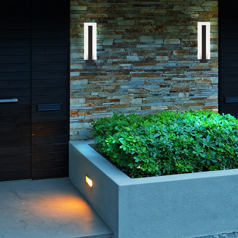 Modern entryway featuring a stone wall, sleek wall-mounted light fixtures, and a landscaped green bush beside a minimalist concrete planter.
