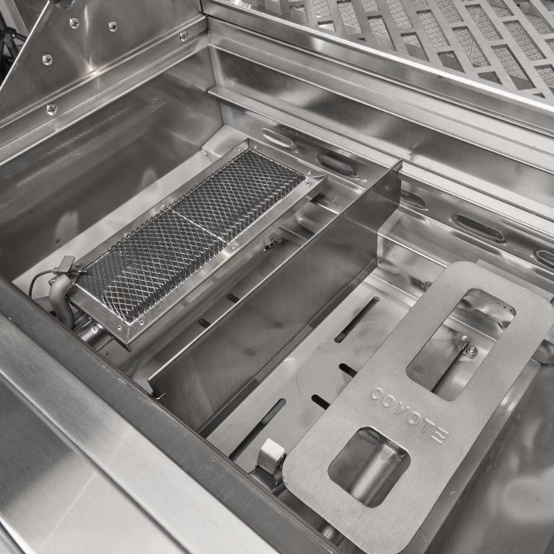 Interior view of a stainless steel grill featuring a mesh burner cover and a Coyote brand plate, designed for efficient grilling.