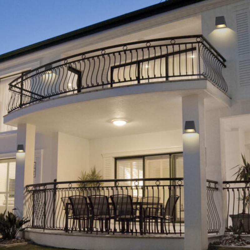 Two-story house exterior featuring a spacious balcony adorned with decorative railings, a round dining table and chairs set below soft outdoor lighting, emphasizing modern architectural design against a twilight backdrop.