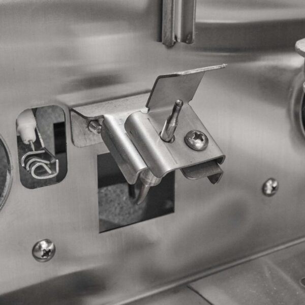 Close-up of a metal hinge and latch mechanism on a stainless steel appliance, showcasing detailed components and mounting features.