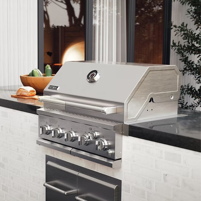 Stainless steel outdoor gas grill with multiple burners, placed on a sleek countertop, surrounded by a bowl of fresh vegetables and a loaf of bread.