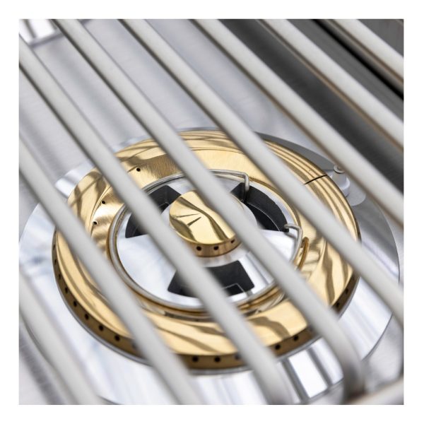 Close-up of a stainless steel gas burner with a gold accent, partially obscured by grill grates, showcasing a modern cooking appliance design.