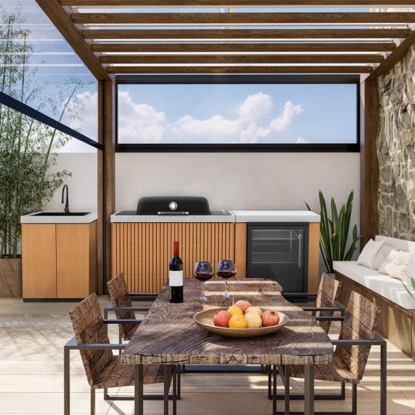 Modern outdoor kitchen setup featuring a wooden dining table with fruit, wine glasses, and a bottle of wine. The kitchen area includes a grill, sink, and refrigerator, surrounded by stylish seating and greenery.