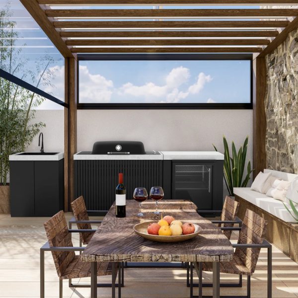 Modern outdoor kitchen with a sleek black grill, sink, and storage, featuring a wooden dining table set with wine glasses and a fruit bowl. The space is enhanced by natural light and greenery, ideal for entertaining.
