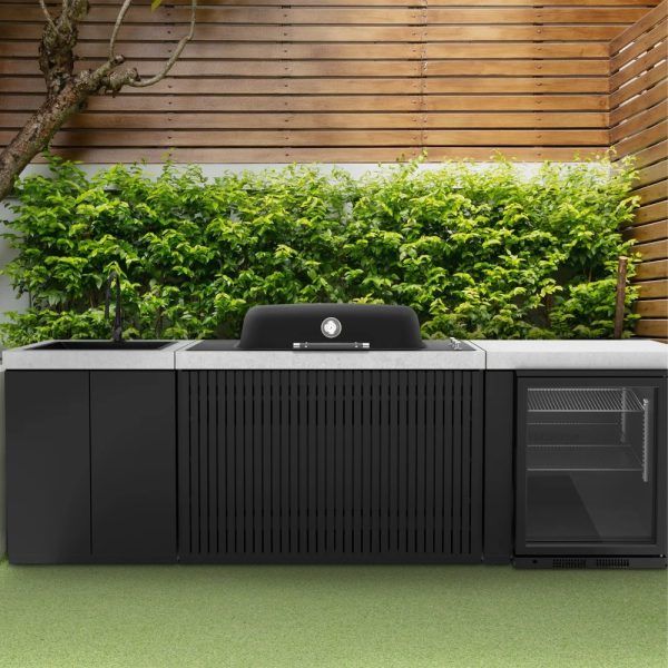 Modern outdoor kitchen featuring a sleek black grill, stone countertop, sink, and a refrigerator, surrounded by lush green foliage and wooden privacy slats.