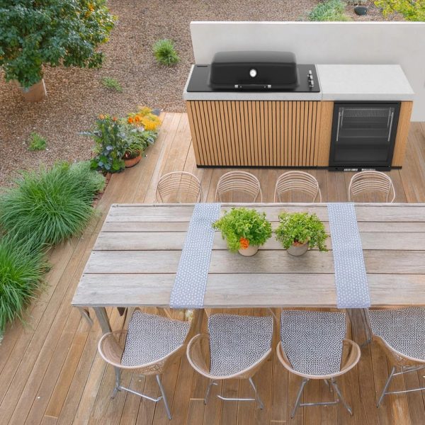Outdoor dining area featuring a modern grill, wooden cabinetry, and a spacious table set with potted plants and stylish seating.