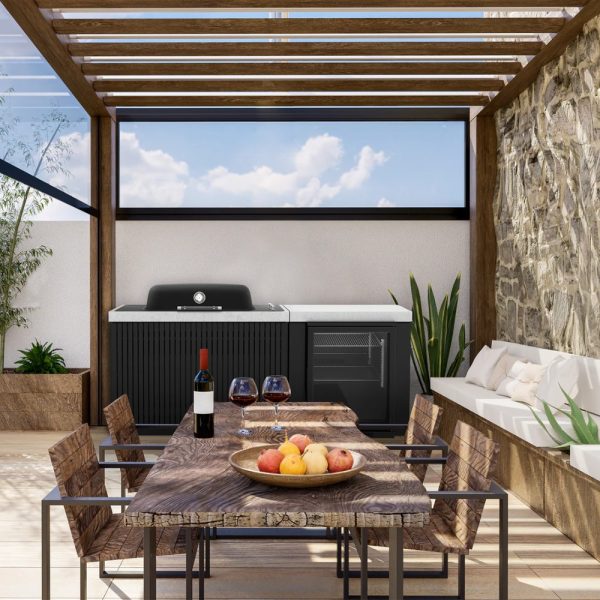 Modern outdoor kitchen setup featuring a grill, wine bottles, and a fruit bowl on a wooden dining table, with a cozy seating area and plants in a stylish pergola.